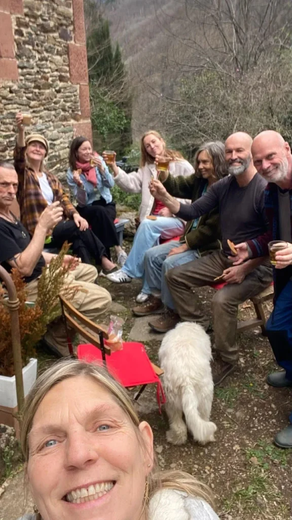 Groep deelgenoten en gasten van La Nouvelle Terre verzameld rond een kampvuur op Domaine du Puech Fleuri, genietend van dranken en gezelschap in de Franse Vallée du Lot.