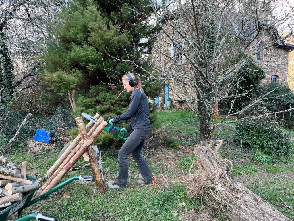 Een vrouw met koptelefoon zaagt houthakkerij uit op het domein van La Nouvelle Terre in de Vallée du Lot, Frankrijk. De werkzaamheden maken deel uit van de regeneratieve landbouw en bosbeheer op het 20 hectare grote landgoed.